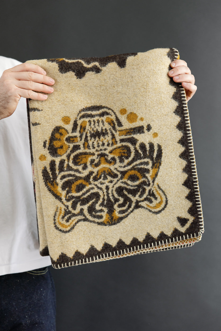 Front view of a patterned wool blanket held by a person against a dark background.