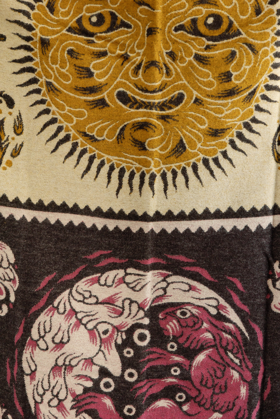 Close-up of fabric texture featuring an intricate gold sun face and red graphic patterns.