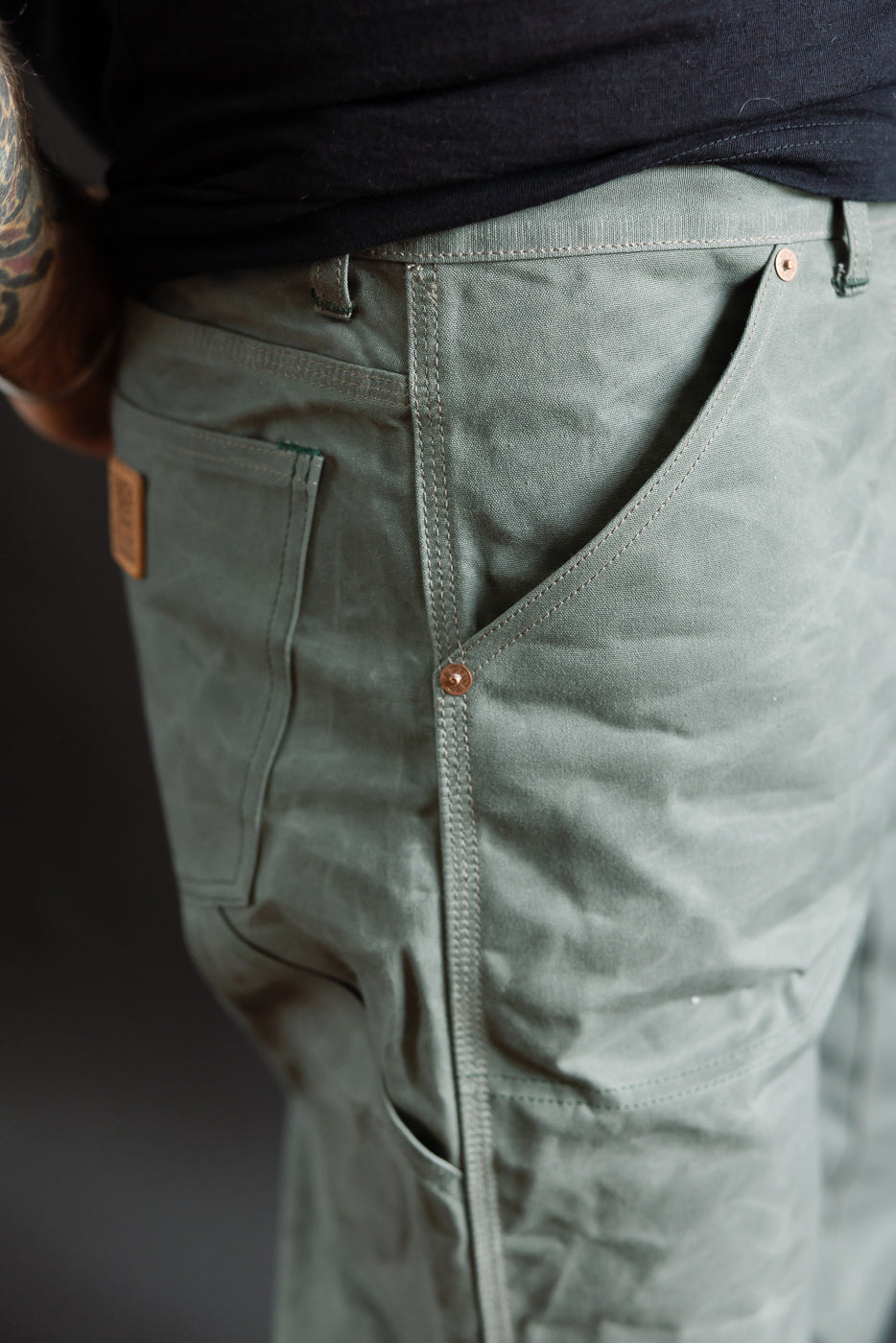 Close-up of double knee pants right side, showing pocket, stitching, and rivet on male model, 5'9