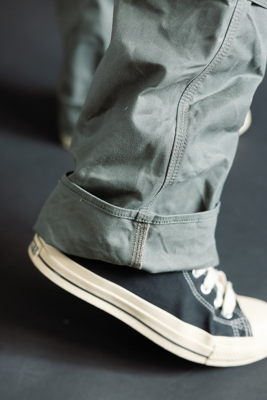 Close-up side view of male model's lower leg in greyish coated canvas double knee pants, hem detail visible, worn by 5'9