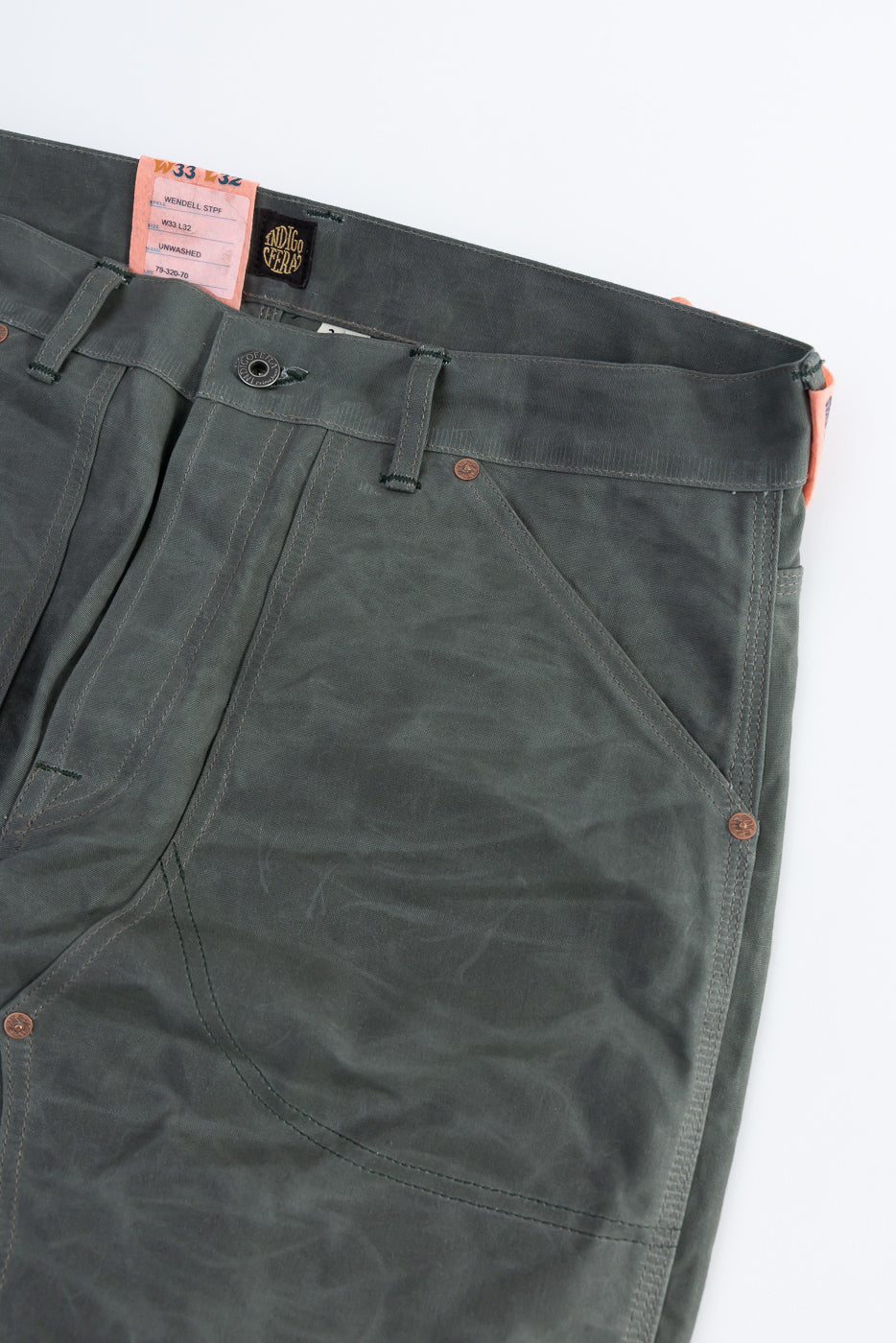 Close-up of front waist and upper thigh of grey coated canvas double knee pants, showing pocket, waistband, button, and fabric texture.