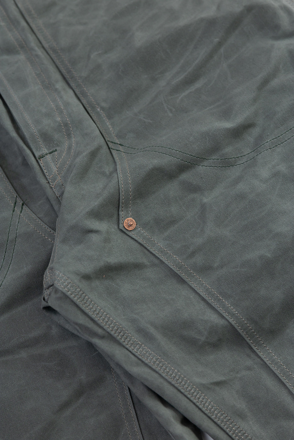 Close-up of front thigh and knee detail on grey coated canvas double knee pants, showing stitching and rivet.