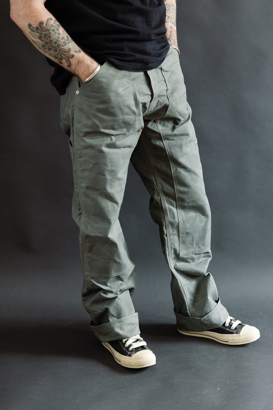 Full body front view of male model 5'9, 165lbs in greyish double knee canvas pants, hands in pockets