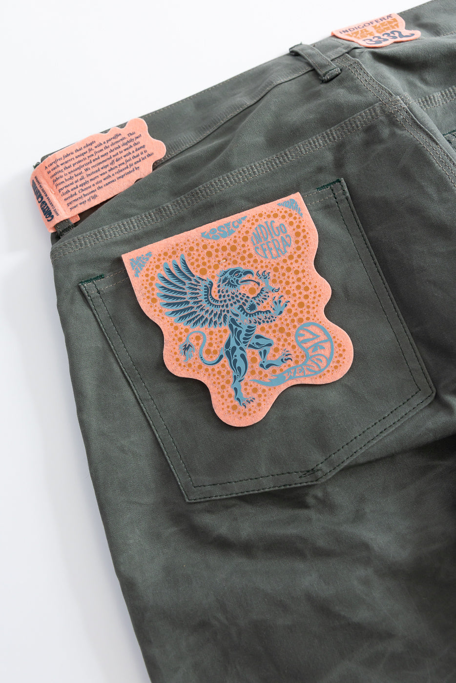 Close-up of back side of greyish coated canvas pants showing pocket detail and graphic tag.