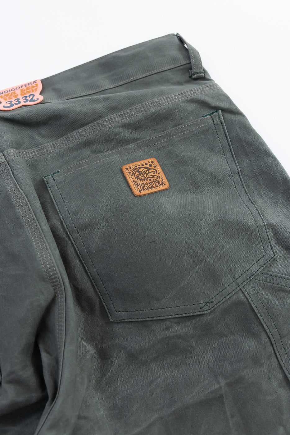 Close-up of the back side of grey coated canvas pants, showing rear pocket, stitching, and leather patch detail.