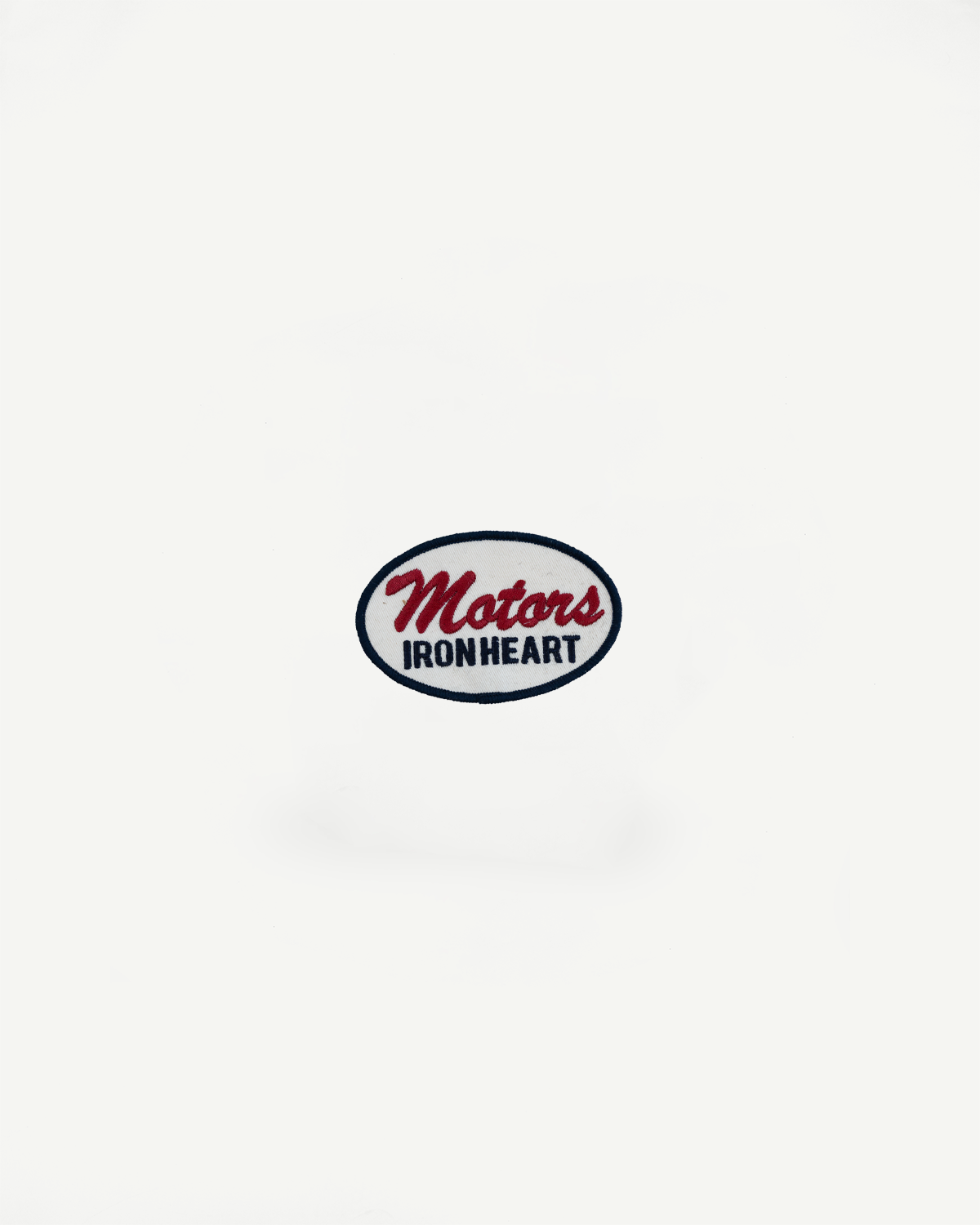 Close-up of Motors Ironheart embroidered patch on white garment, front view, oval design with red and navy text.