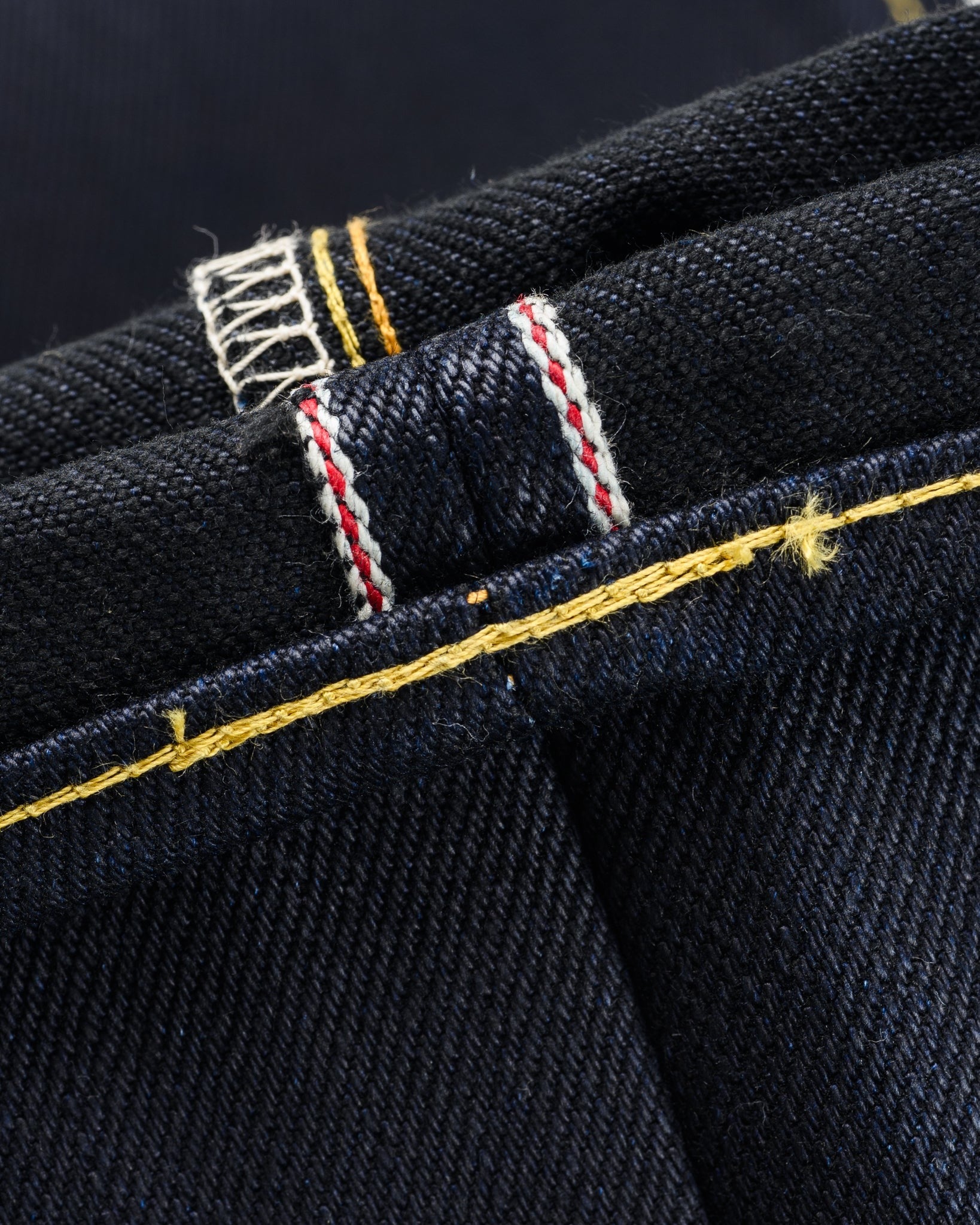 Close-up of Iron Heart IH-634-XHSib 25oz selvedge denim hem, showing indigo-black fabric and detailed yellow and white stitching at seam.