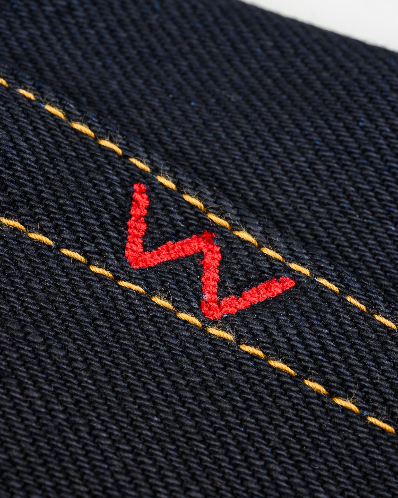 Close-up of Iron Heart IH-634-XHSib 25oz selvedge denim fabric with red embroidery and yellow stitching detail, front view.
