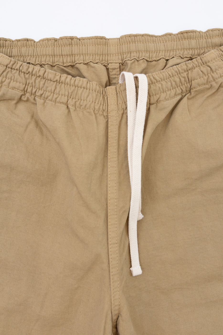 Close-up front view of tan drawstring shorts, elastic waistband, white cord, fabric texture visible