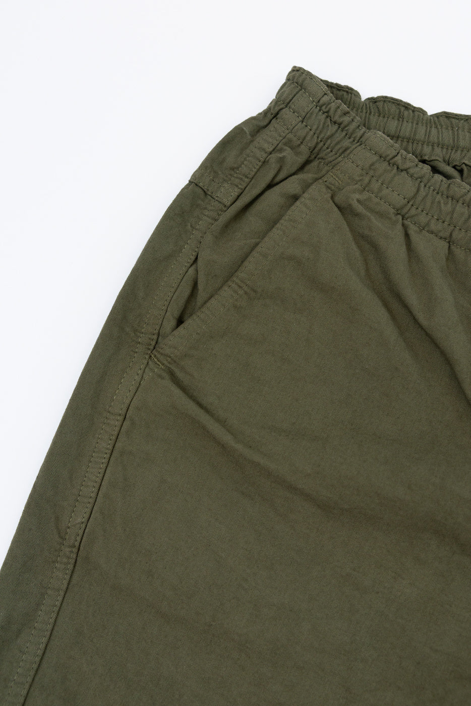 Close-up front view of olive green casual pants showing elastic waistband and side seam detail