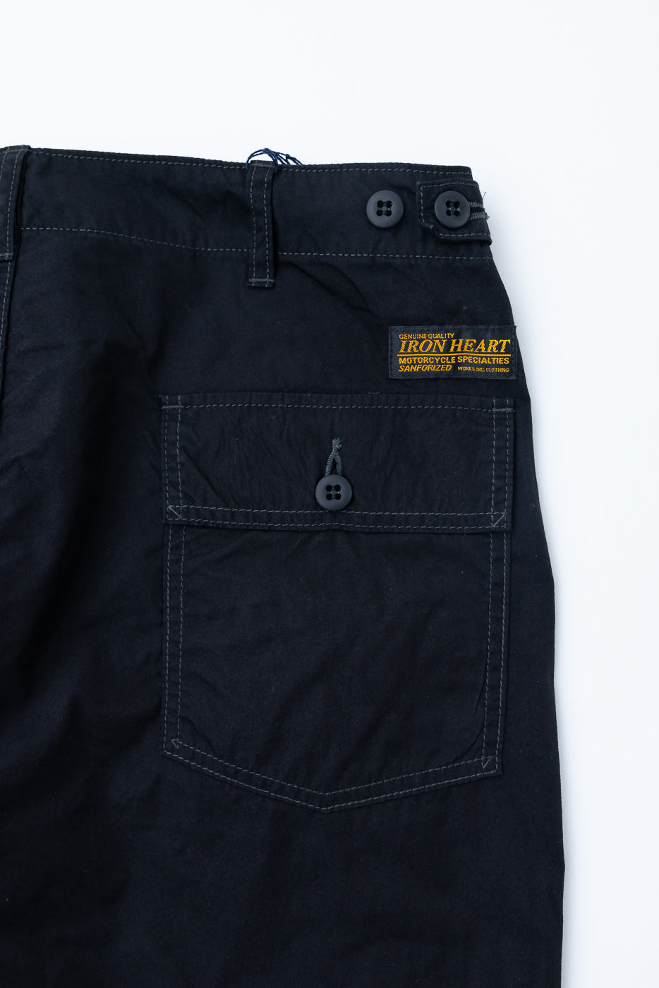 Close-up front view of black pants with buttoned pocket, tag, and stitching details