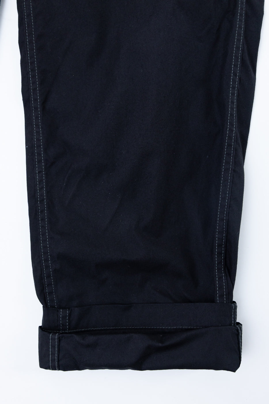 Close-up front view of black pants with cuffed hem and contrast stitching