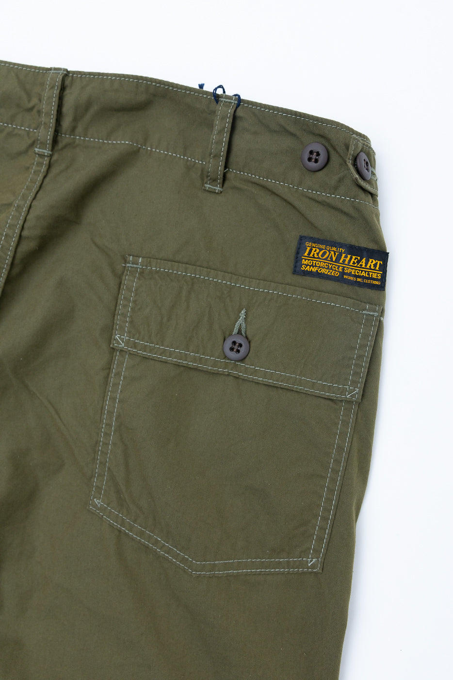 Close-up of olive green cargo shorts front, showing buttoned pocket, stitching, and Iron Heart label.