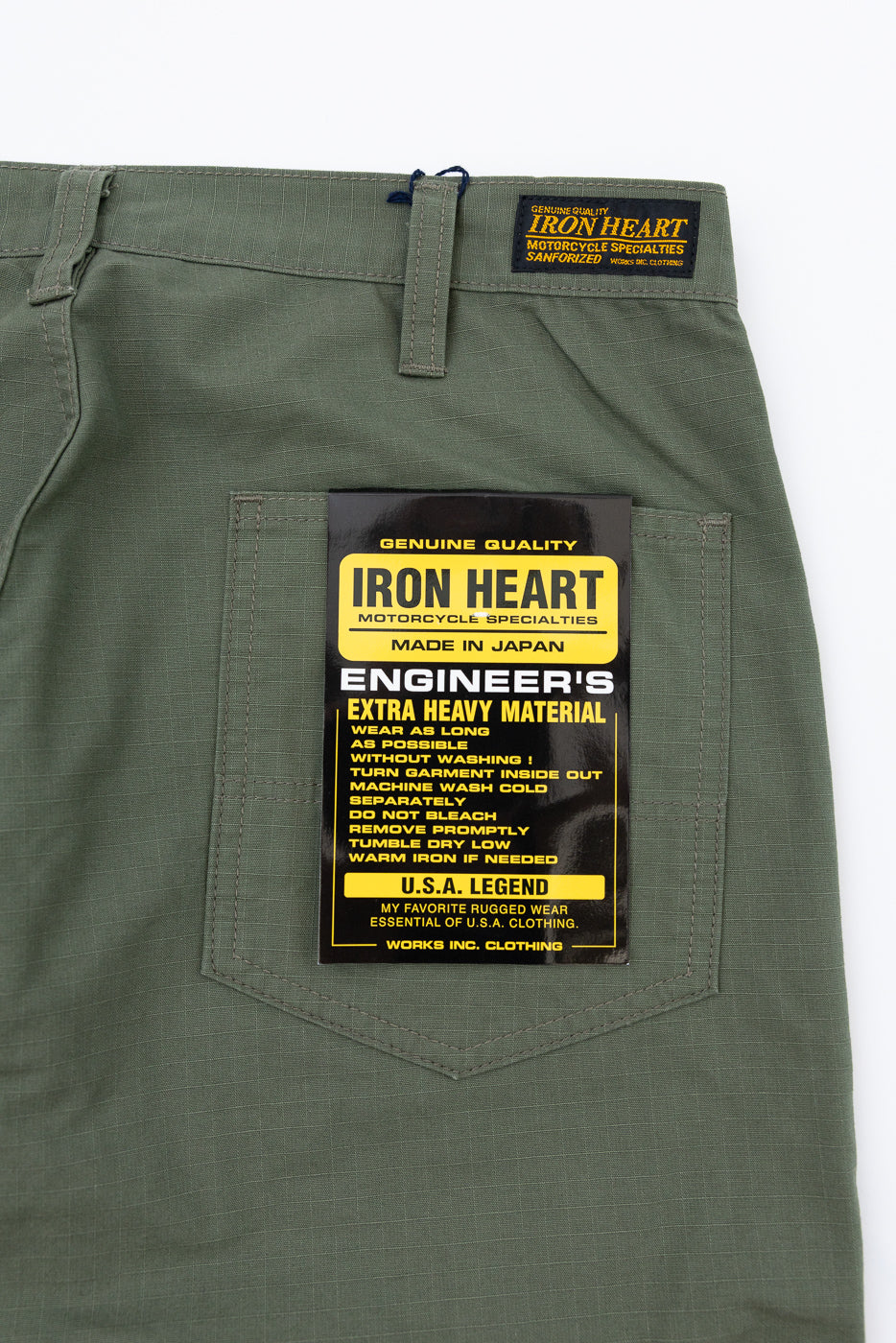 Close-up front view of olive green Iron Heart Engineer's pants, showing back pocket label with 'Made in Japan' and care instructions.