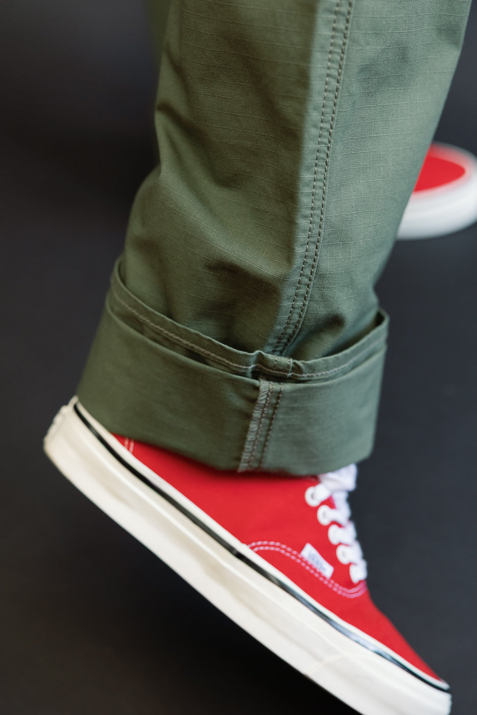 Close-up side view of olive green pants hem with cuffed detail, worn by male model, paired with red sneakers