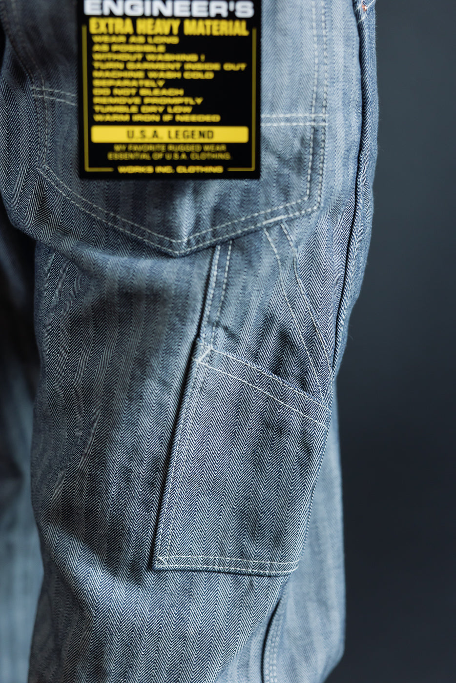 Close-up of men's engineer jeans back pocket with herringbone selvedge fabric, white stitching, and care label detail
