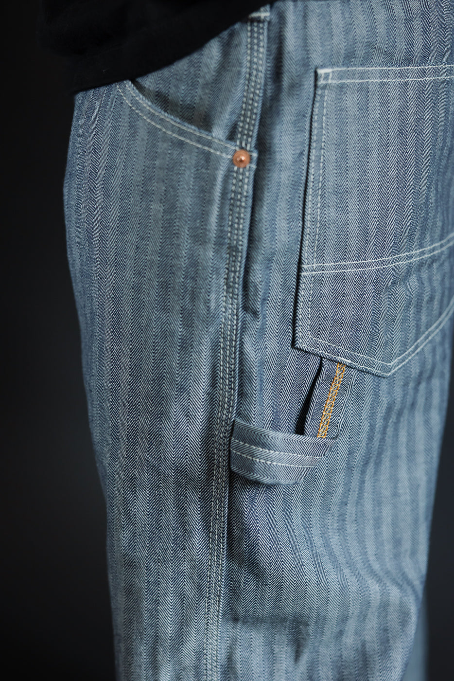 Close-up of men's herringbone selvedge jeans, side view showing back pocket, copper rivet, and contrast stitching