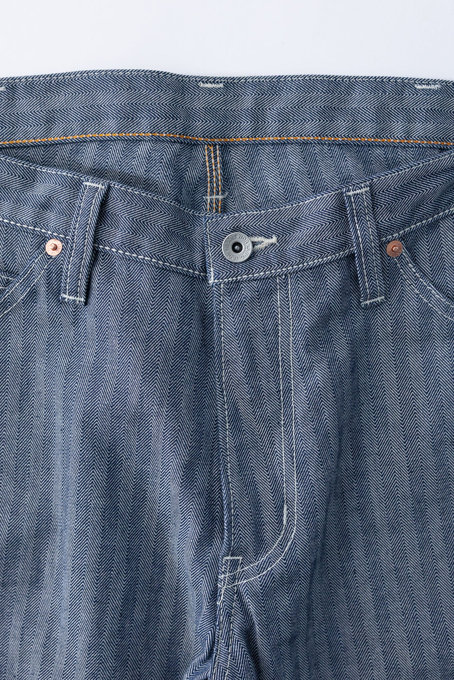 Close-up front view of selvedge denim pants with herringbone texture, button fly, and copper rivets