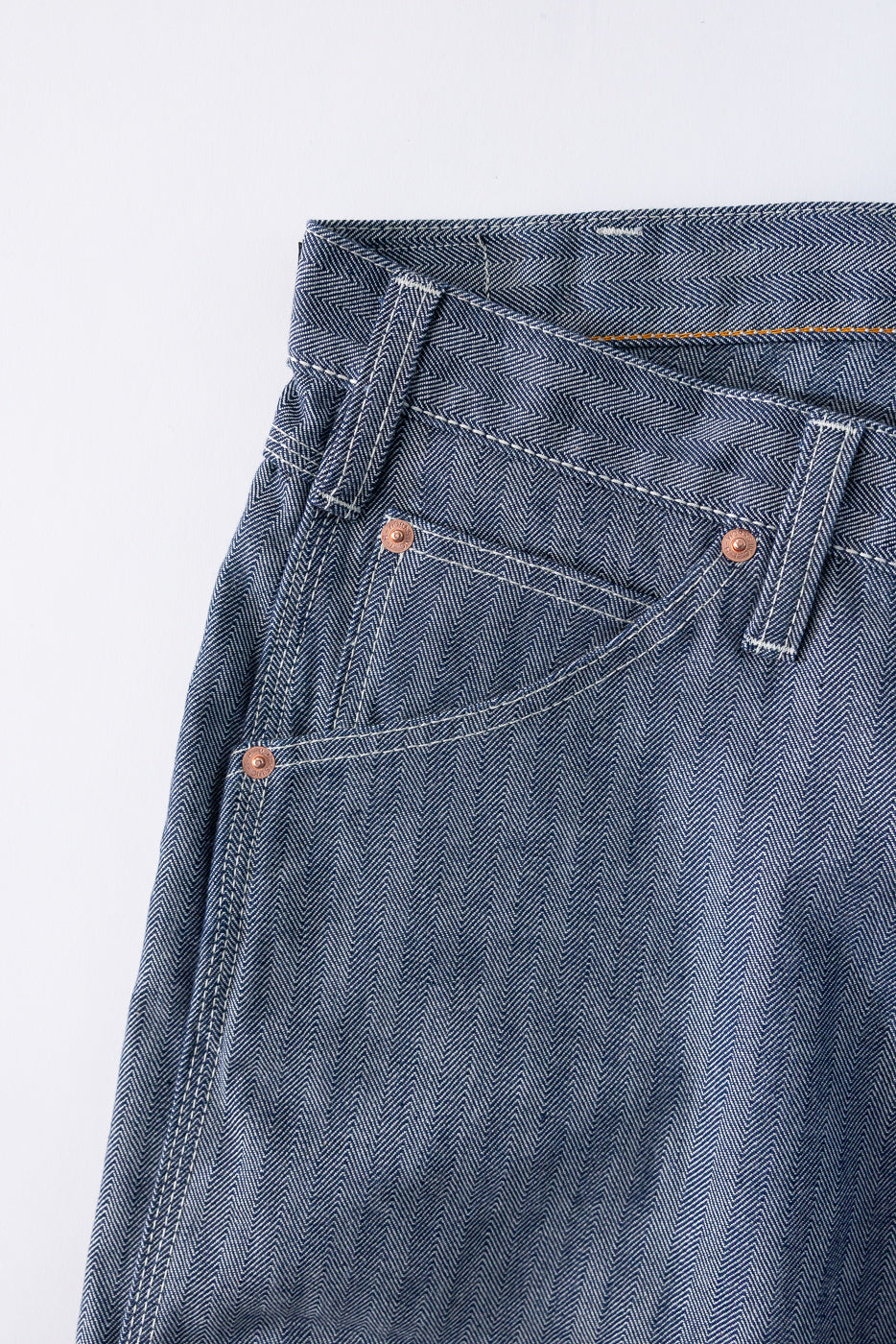 Close-up front view of selvedge denim jeans with herringbone texture, copper rivets, and white stitching