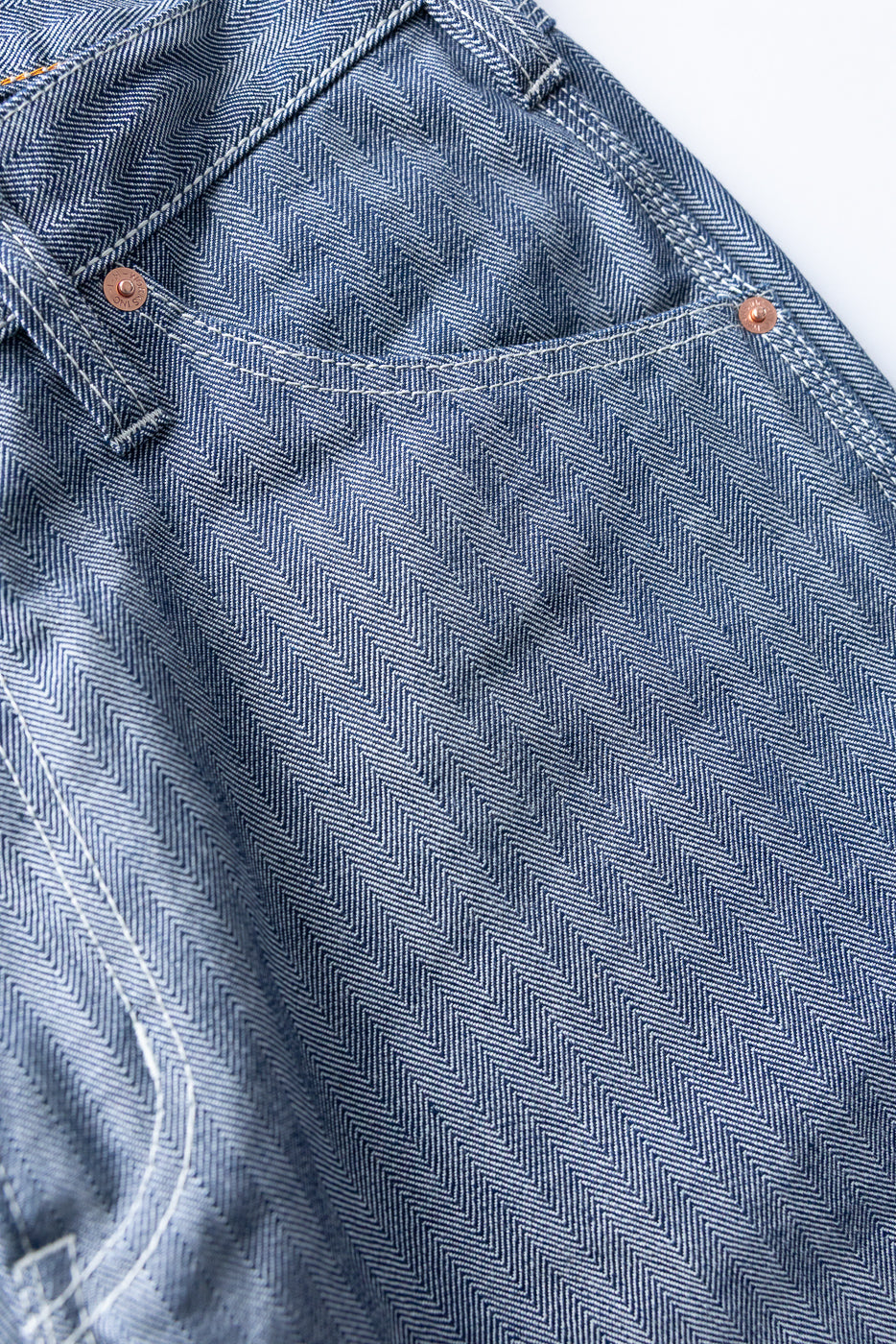 Close-up front view of herringbone selvedge denim with copper rivets and white stitching