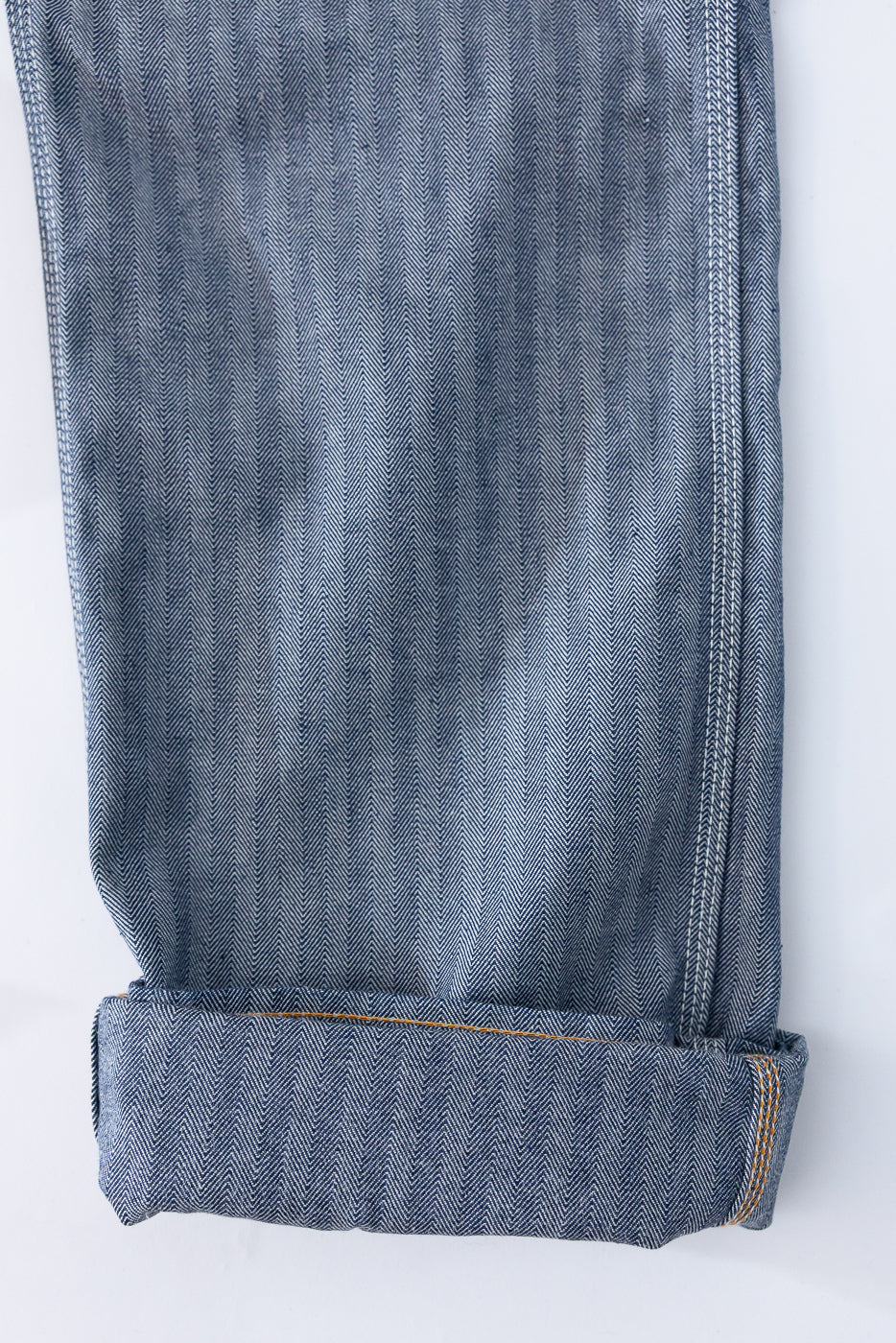 Close-up of selvedge denim pants hem, showcasing herringbone texture and orange stitching detail.