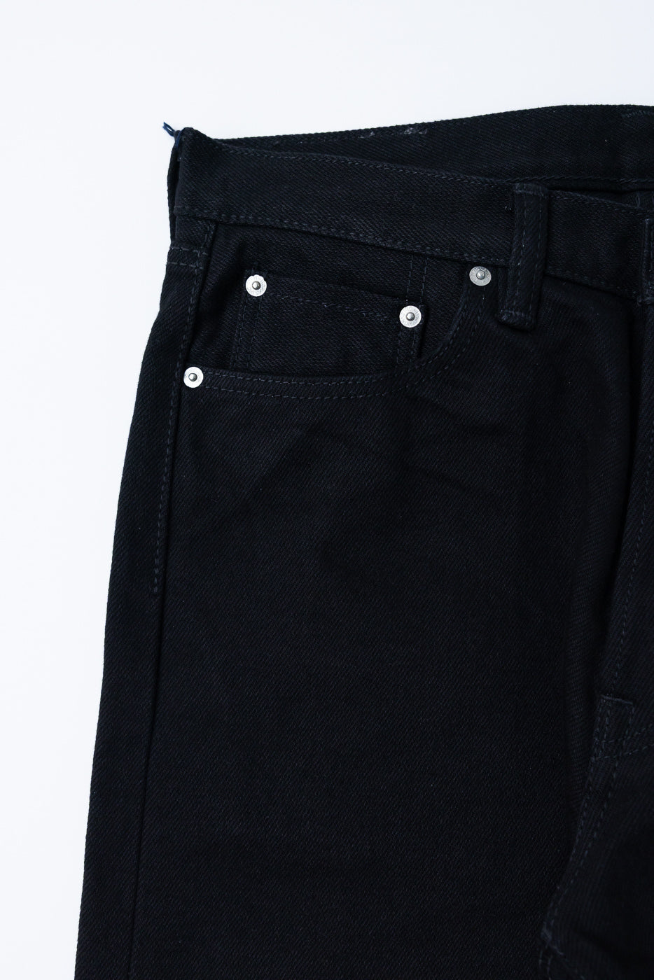 Close-up front view of black selvedge jeans showing button fly, silver rivets, and denim texture