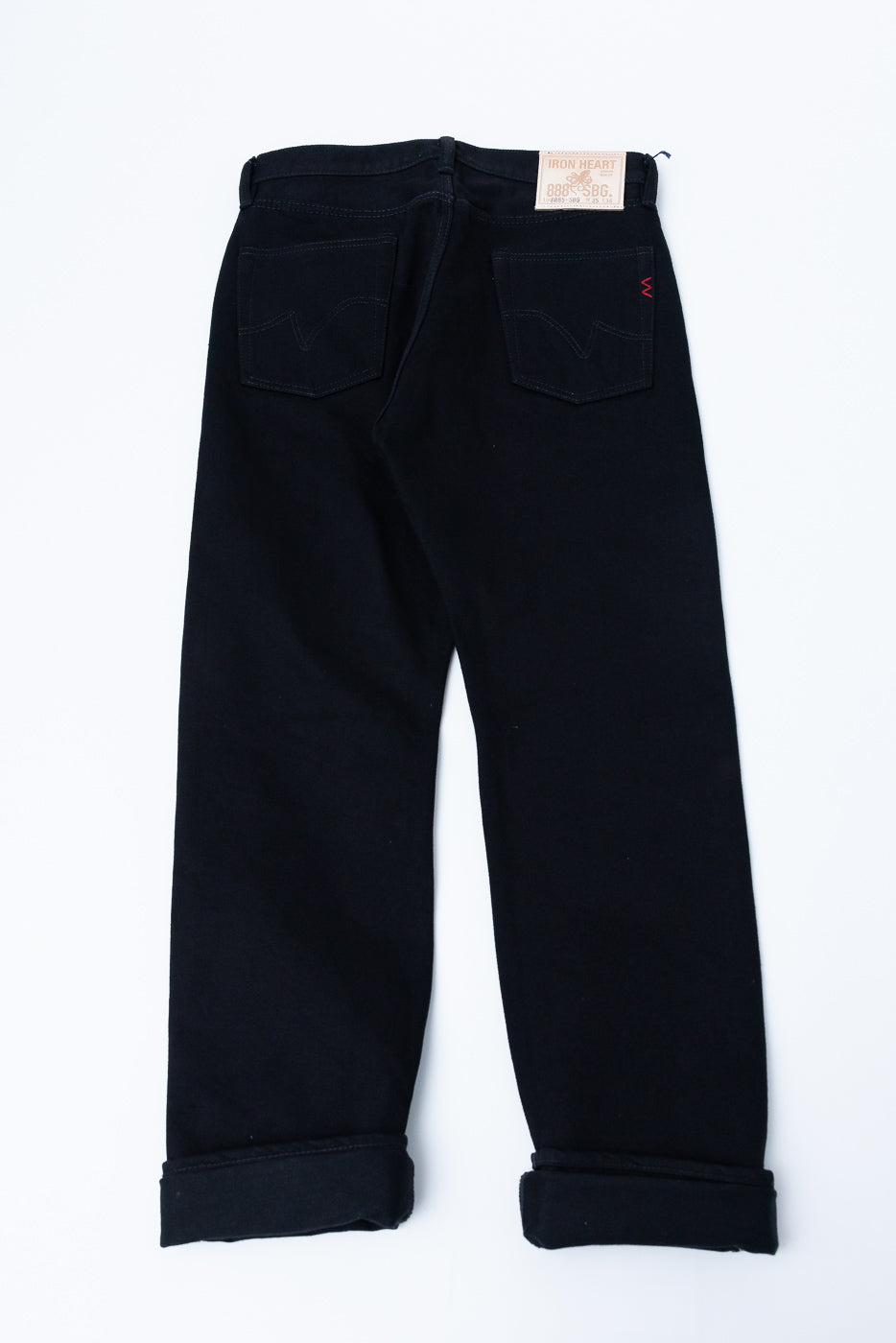 Back view flat lay of black selvedge jeans, cuffed hems, Iron Heart label, red stitching detail