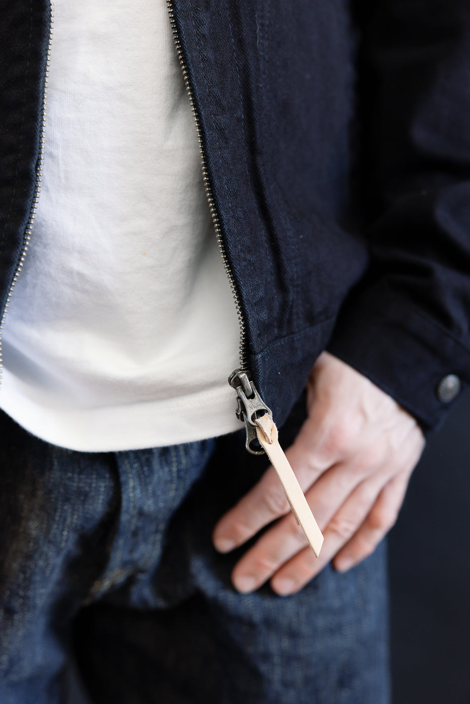 Close-up of the IHJ-123-OD - 14oz Broken Twill Selvedge Denim Work Jacket, revealing its indigo-overdyed black finish, two-way YKK zipper with leather pull, and paired with a white T-shirt.