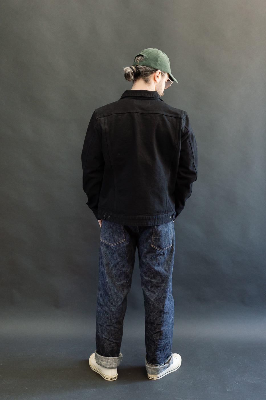 Person wearing IHJ-123-OD - 14oz Broken Twill Selvedge Denim Work Jacket, showcasing its sleek black finish, over blue jeans and white sneakers, embodying Dant's minimalist, heritage-inspired style.