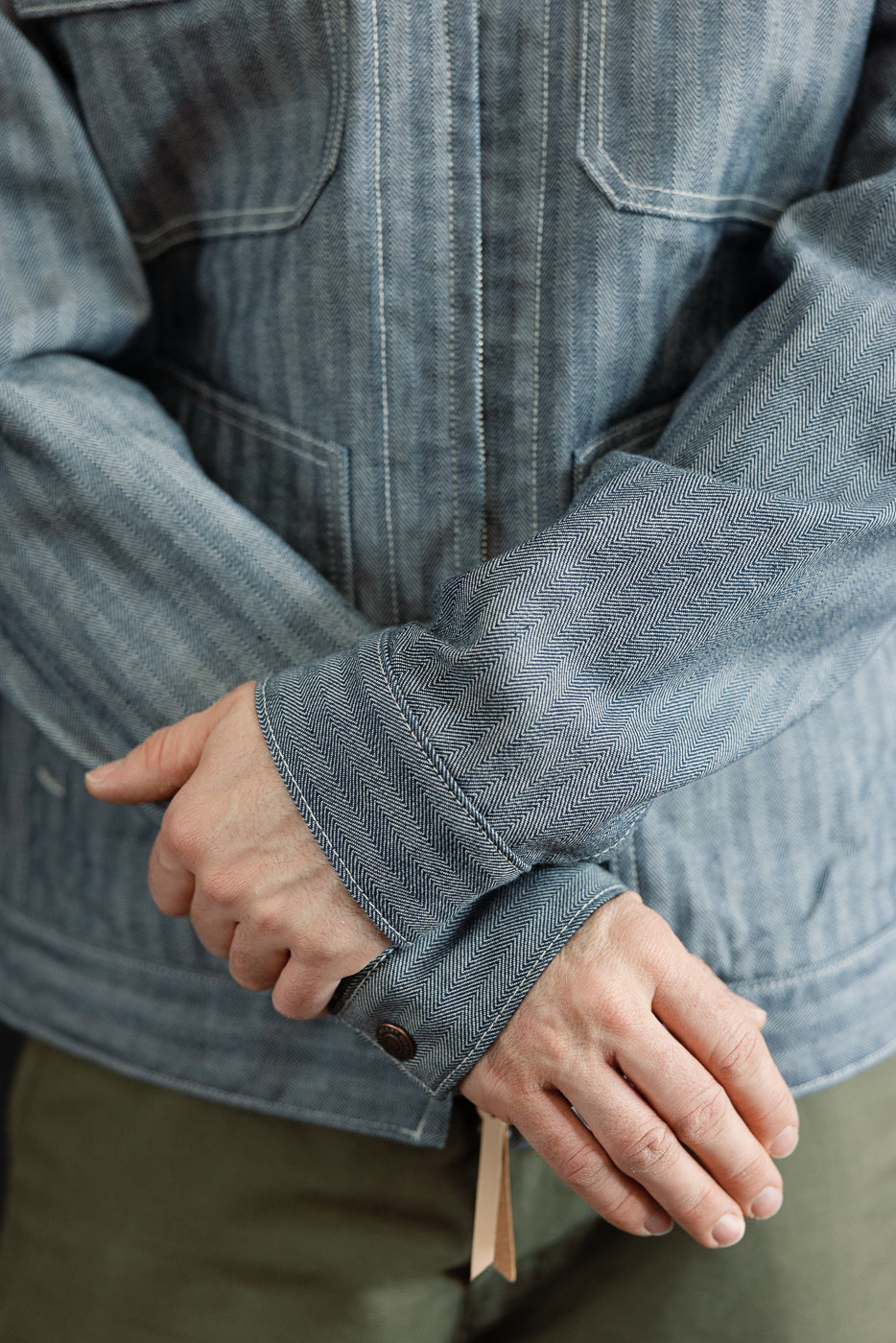 Close-up of cuff and sleeve details on front of indigo herringbone work jacket, male model 5'9, 165lbs, athletic build