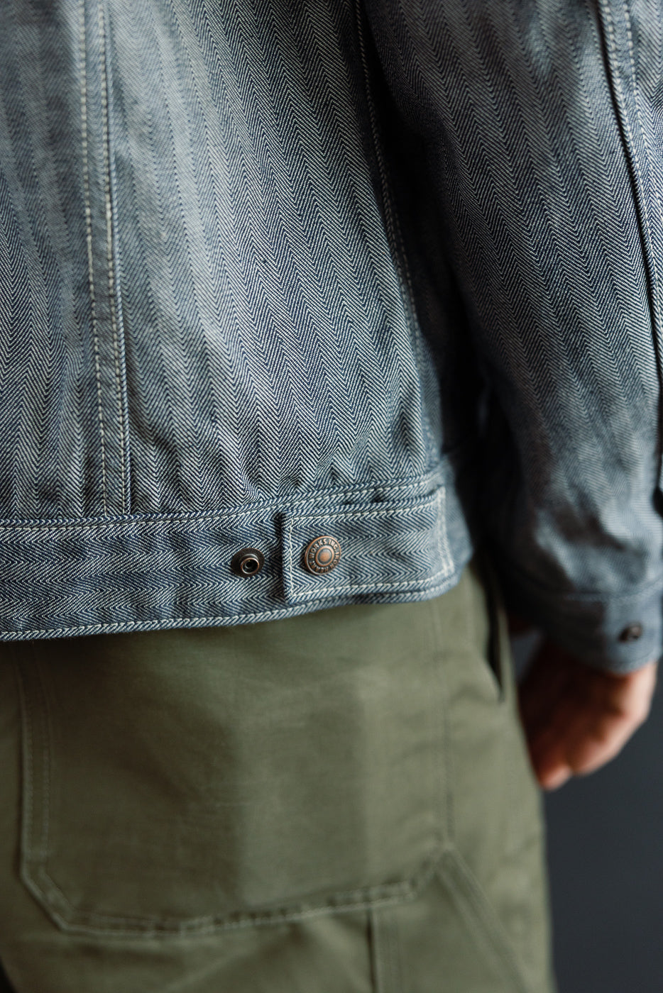 Close-up of back hem on indigo herringbone work jacket, metal button, male model, size reference