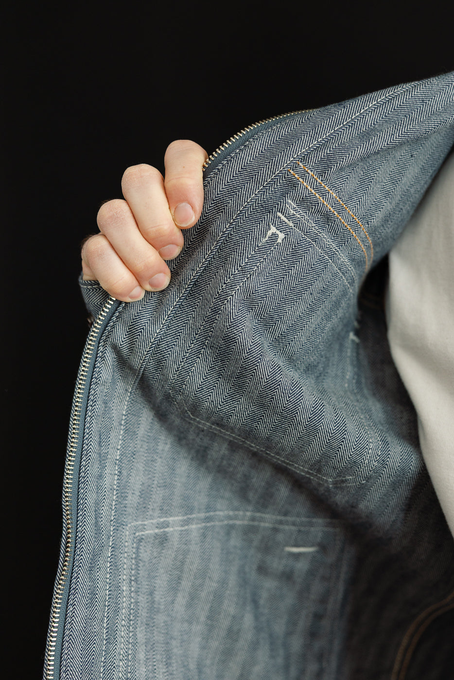 Close-up of male model holding open indigo herringbone work jacket showing inside fabric.