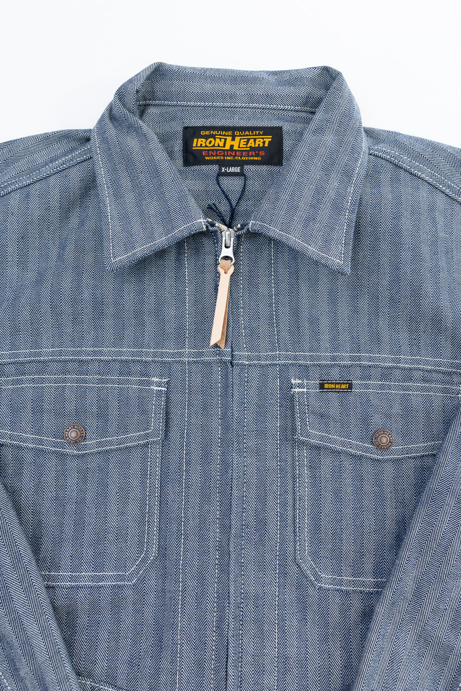 Close-up front view of indigo herringbone work jacket, showing collar, zipper, chest pockets, and tag details.