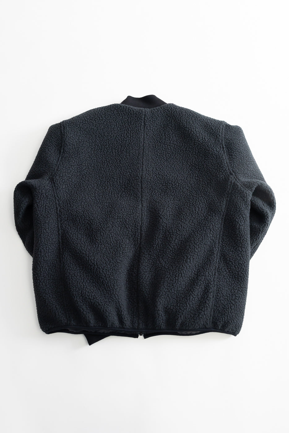 Flat lay of black fleece jacket showing the back, textured fabric, ribbed collar detail.
