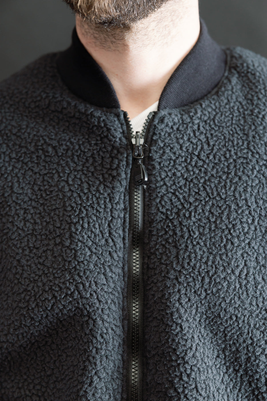 Close-up of front chest and collar of black sherpa fleece jacket on male model, showing zipper and collar details, model is 5'9