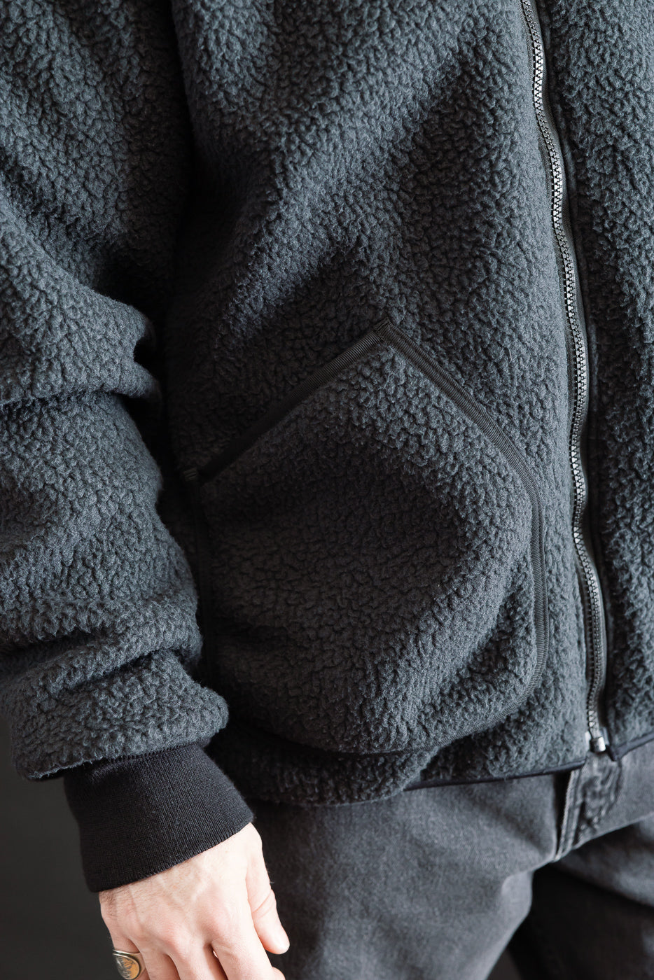 Close-up of front left side of black fleece jacket on male model, showing zip and pocket detail.