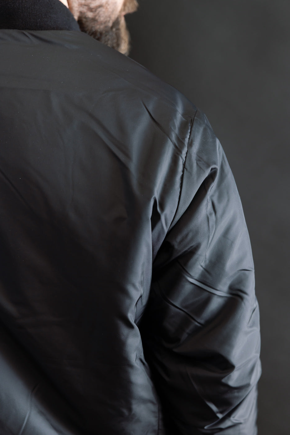 Close-up of male model’s upper back and shoulder in black reversible fleece jacket, showcasing fabric texture.