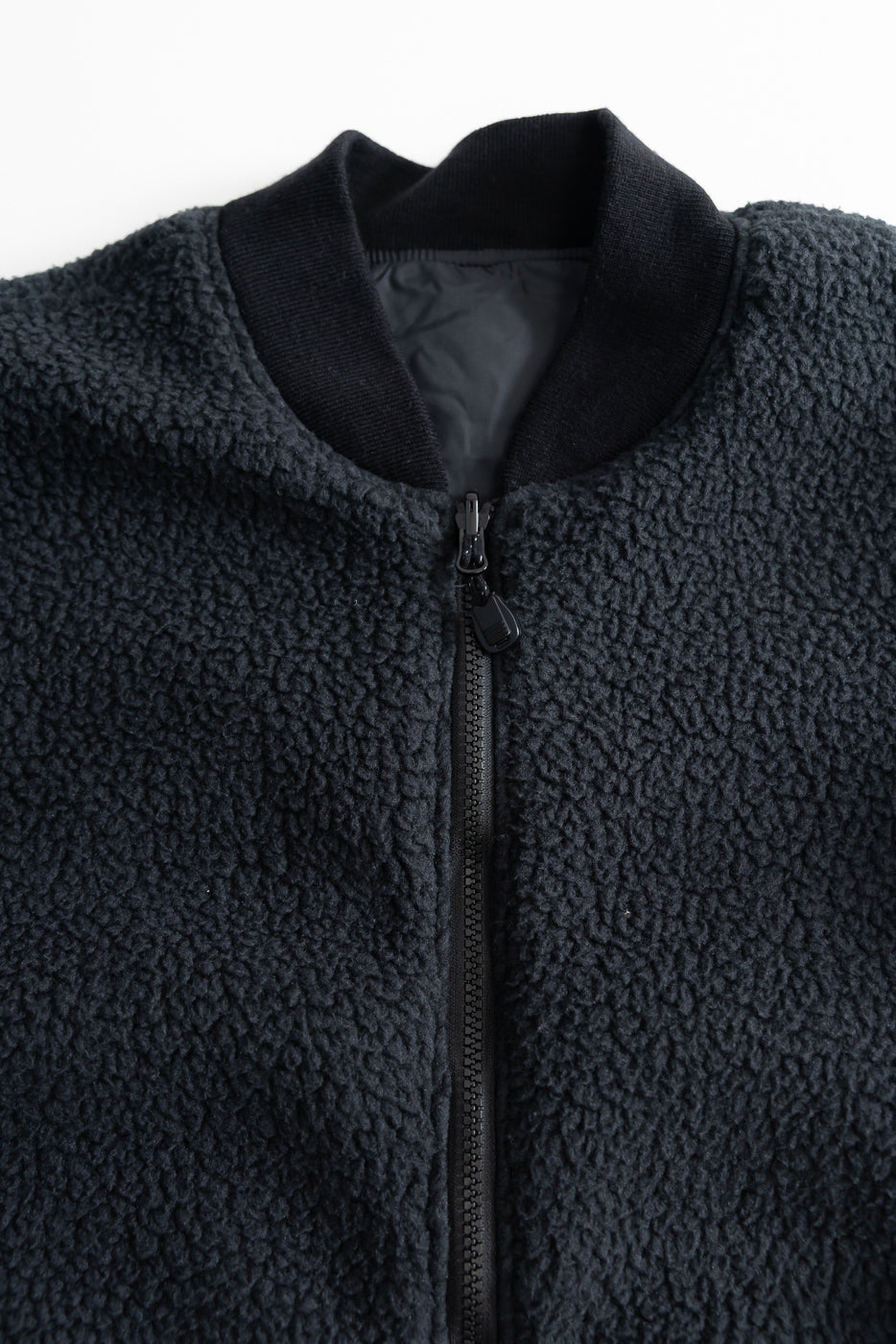 Close-up of front chest and collar of black reversible fleece jacket, showing zipper, ribbed collar, and textured fleece fabric.