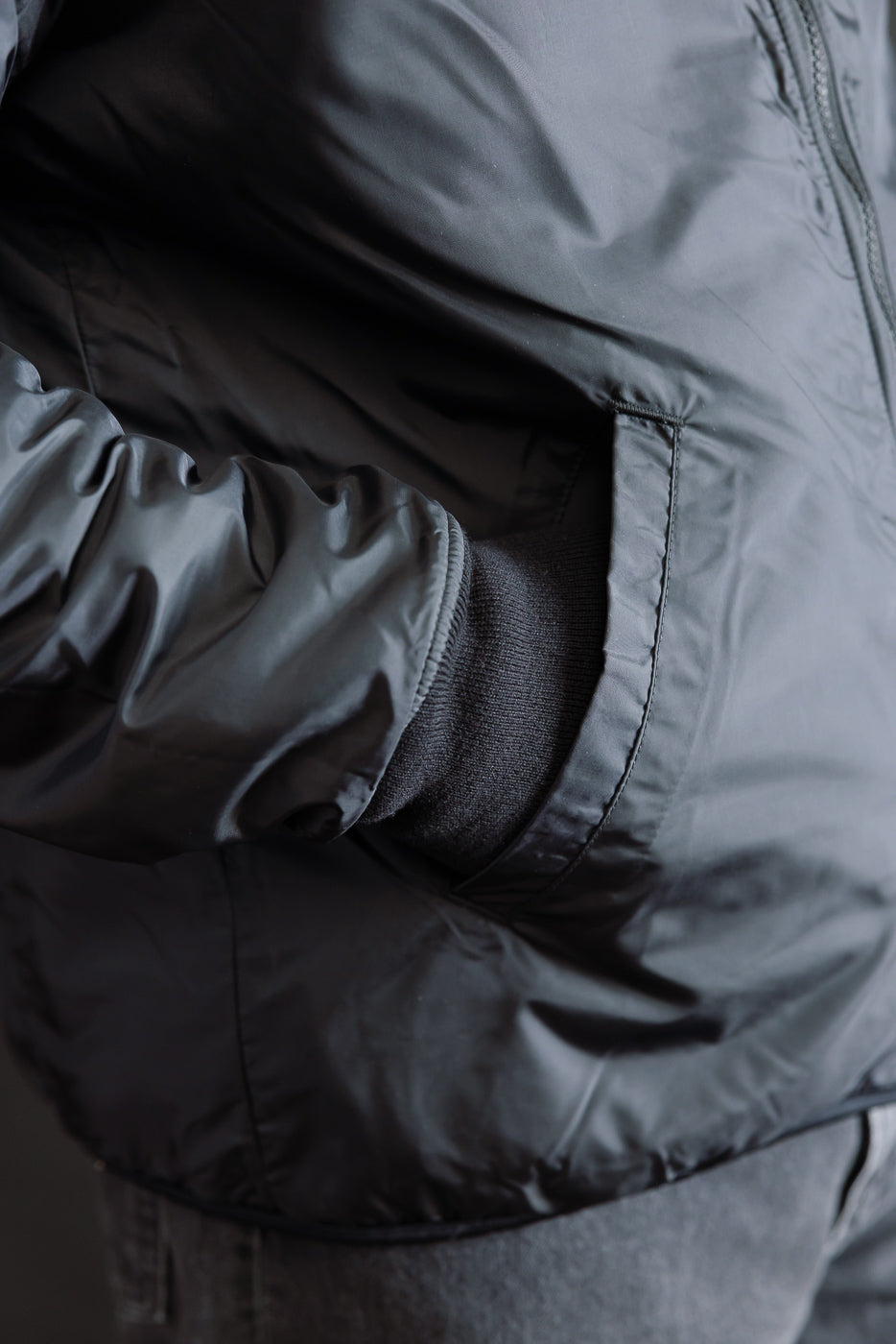Close-up of male model's right hand in pocket of black reversible fleece jacket, front side view, showing fabric texture and ribbed cuff detail.