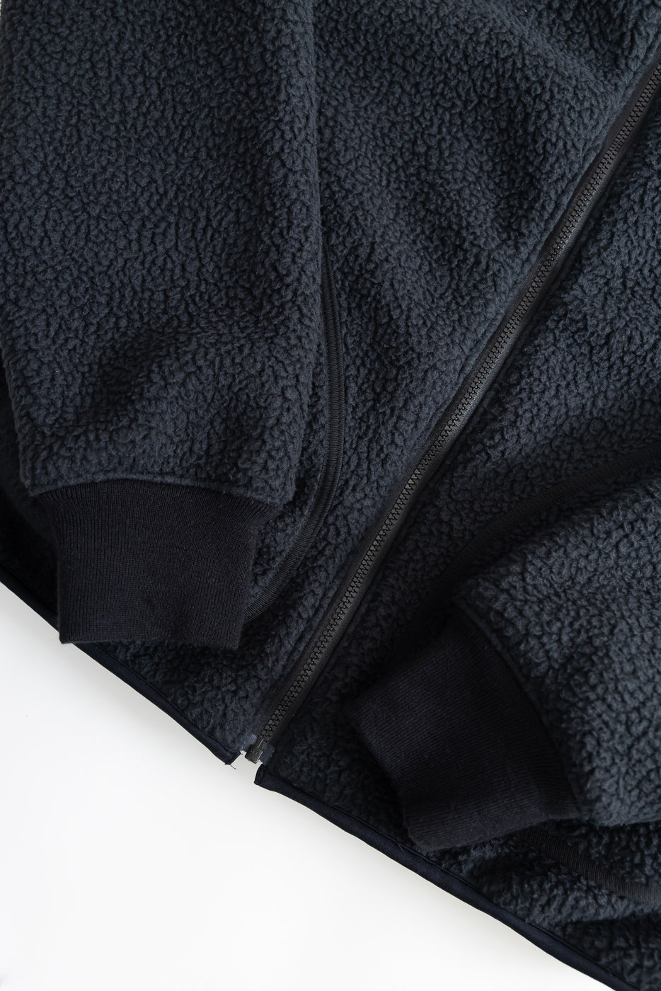 Close-up of black fleece jacket front, highlighting zipper, sleeve cuffs, and textured fabric.