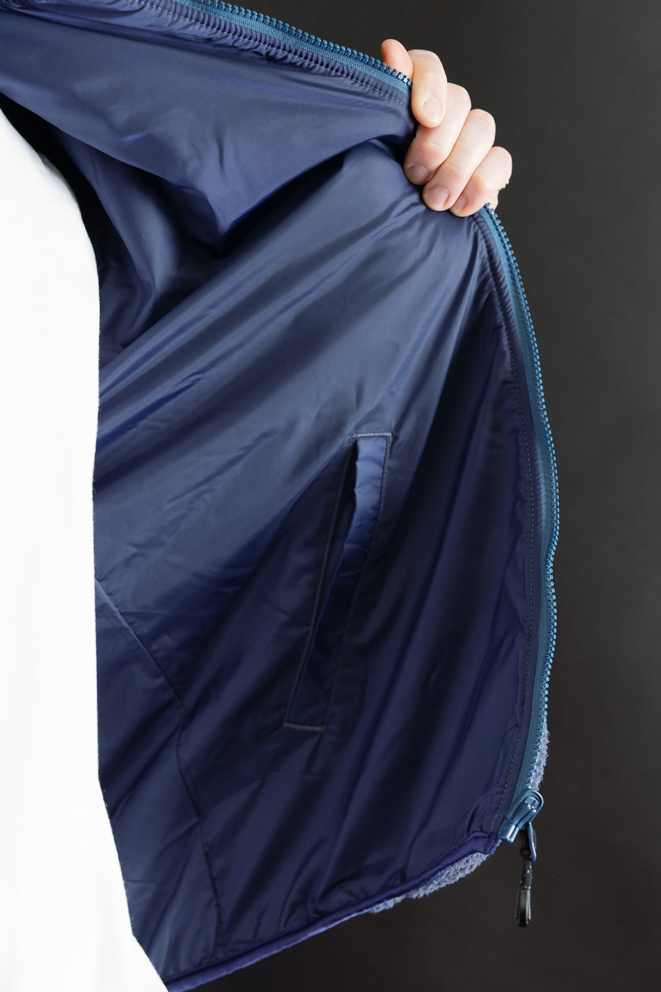 Close-up of the inside front left panel of a navy reversible fleece jacket showing inner pocket and blue lining.