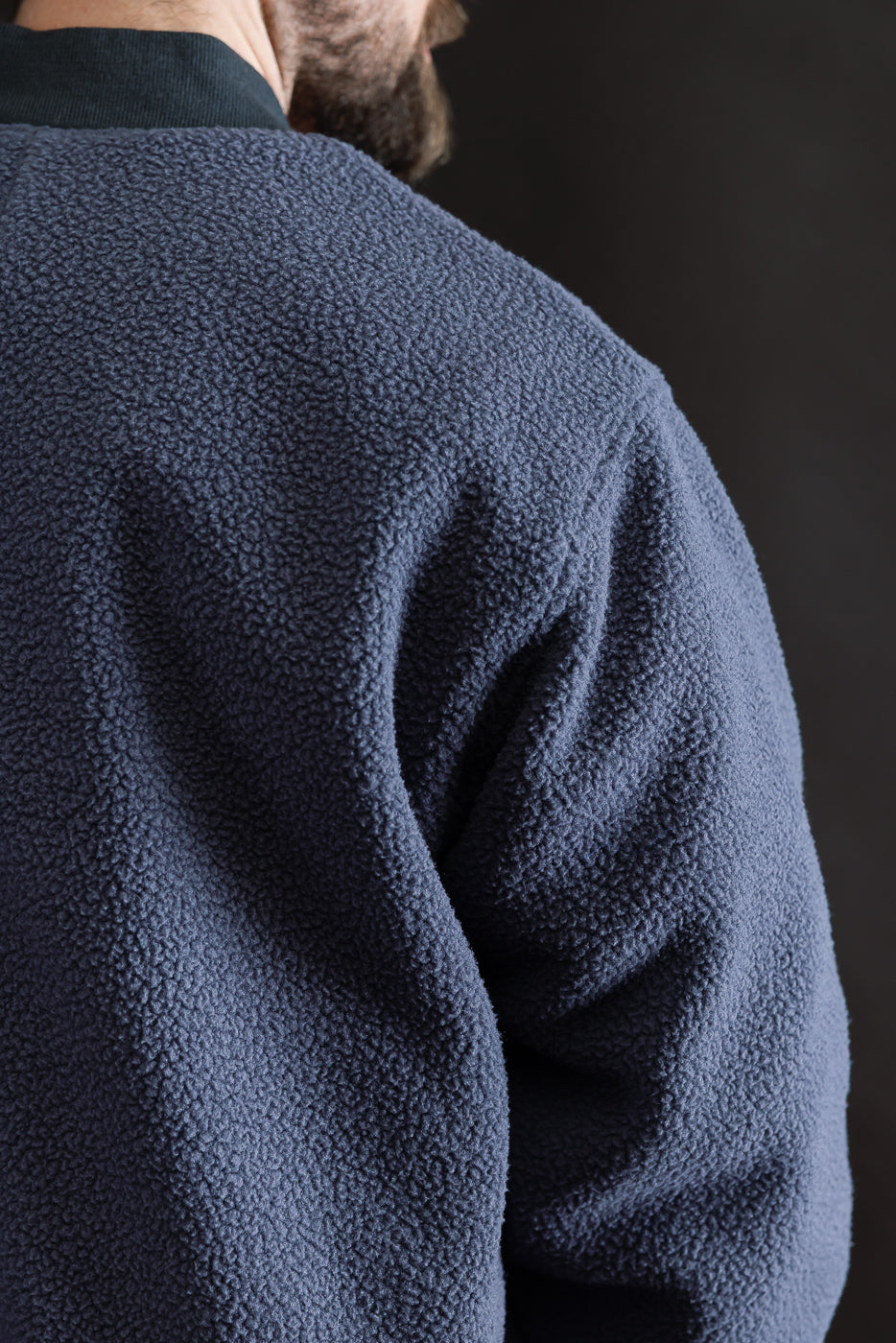 Close-up of back left shoulder and sleeve texture, navy fleece jacket on male model, 5'9