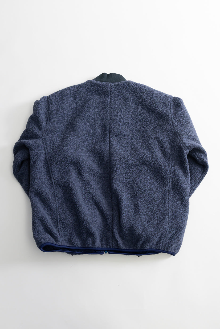 Flat lay of navy reversible fleece jacket, showing back side, textured fabric, elastic hem.