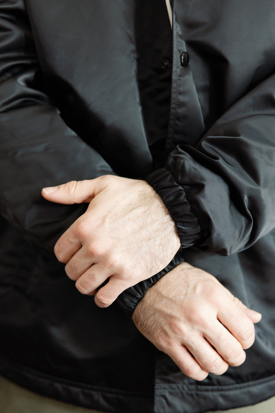 Close-up front view of black nylon coach jacket elastic cuffs on male model, 5'9
