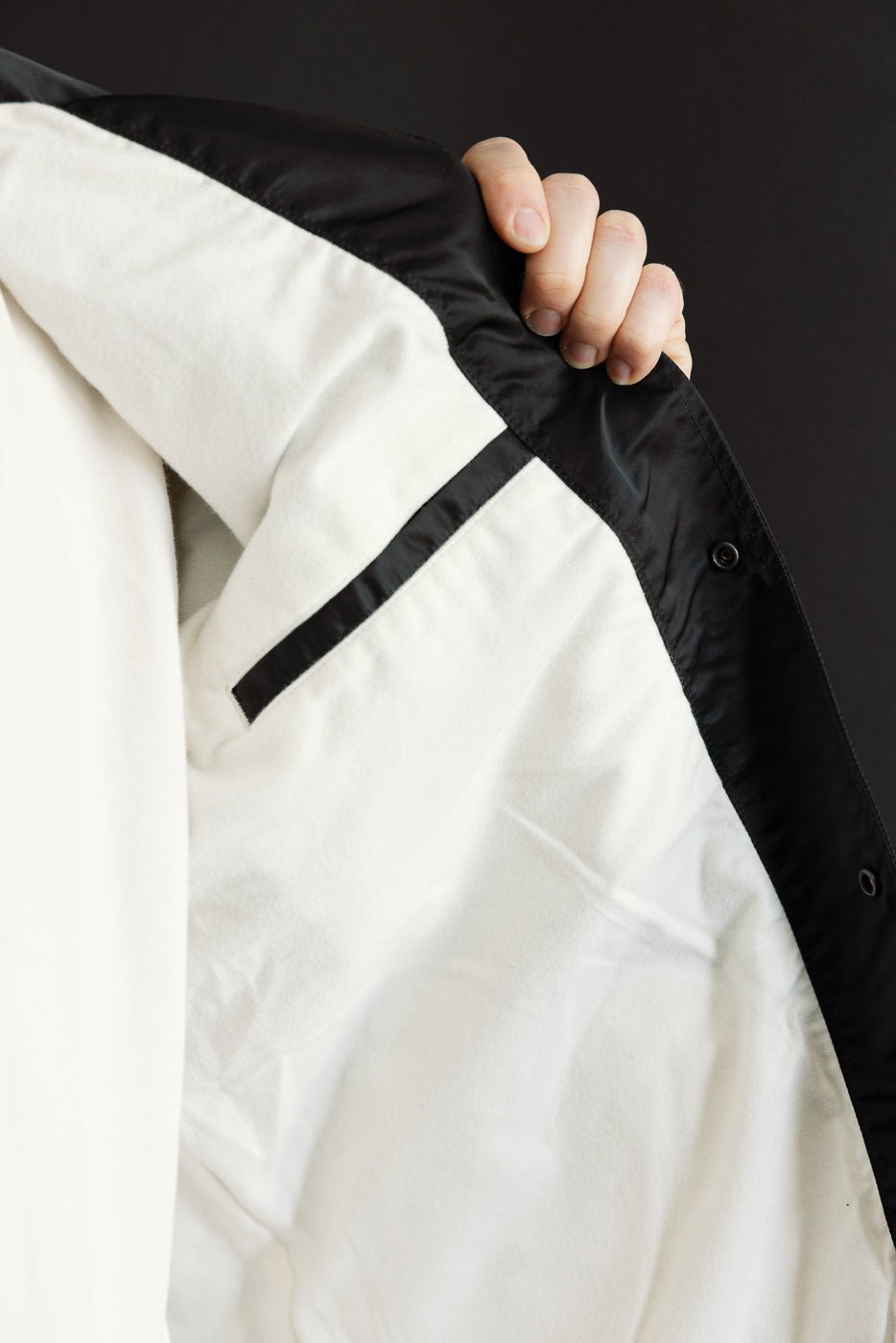 Close-up of inside front of black nylon coach jacket showing white lining and inner pocket.