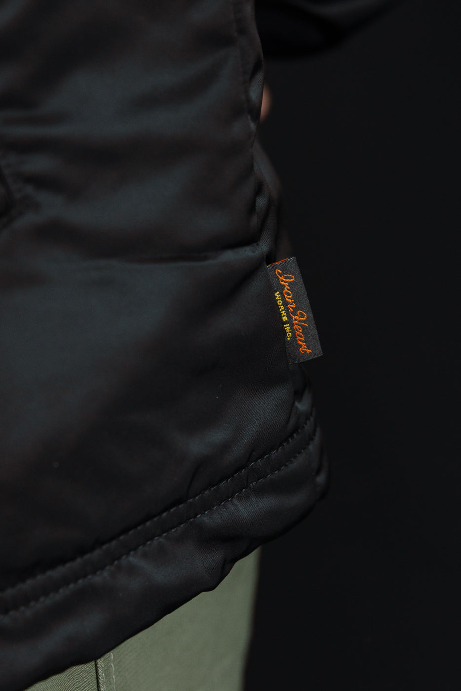 Close-up of lower side hem on black nylon coach jacket, focusing on brand tag detail.