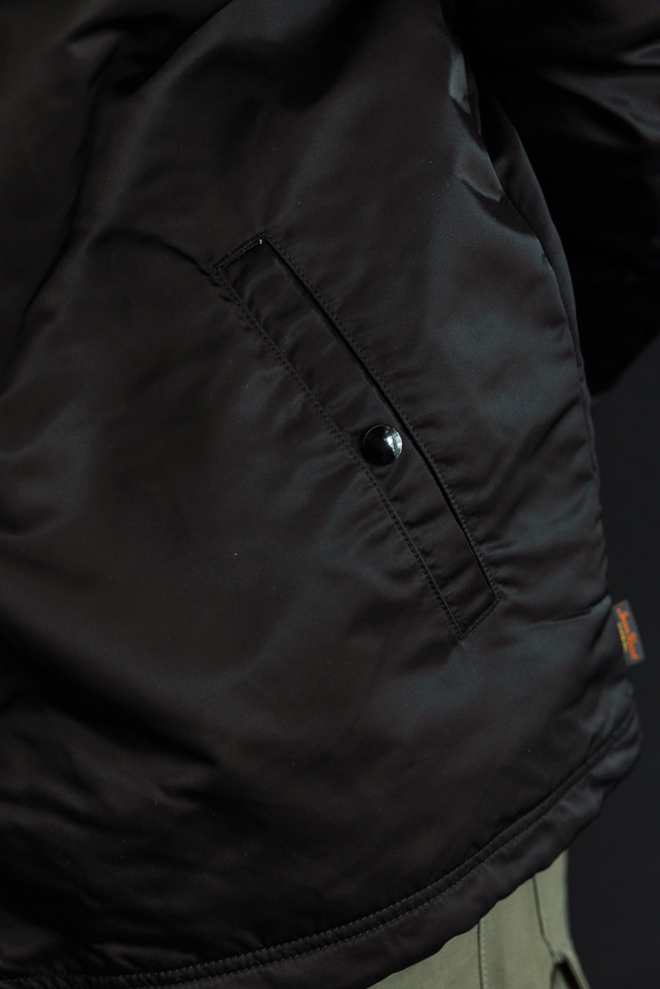 Close-up of black nylon coach jacket front left pocket with snap button and fabric texture