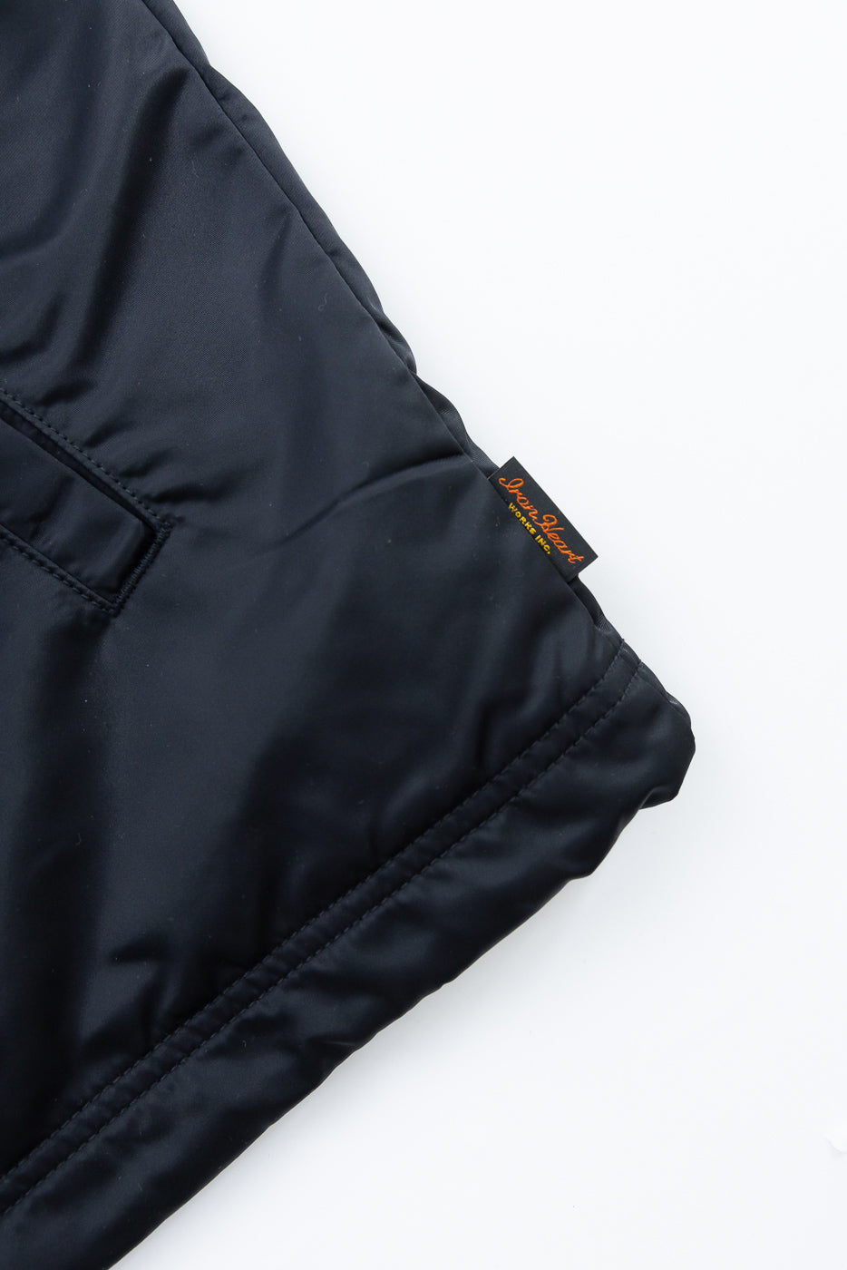 Close-up of black nylon coach jacket hem, side view, showing tag and pocket detail.