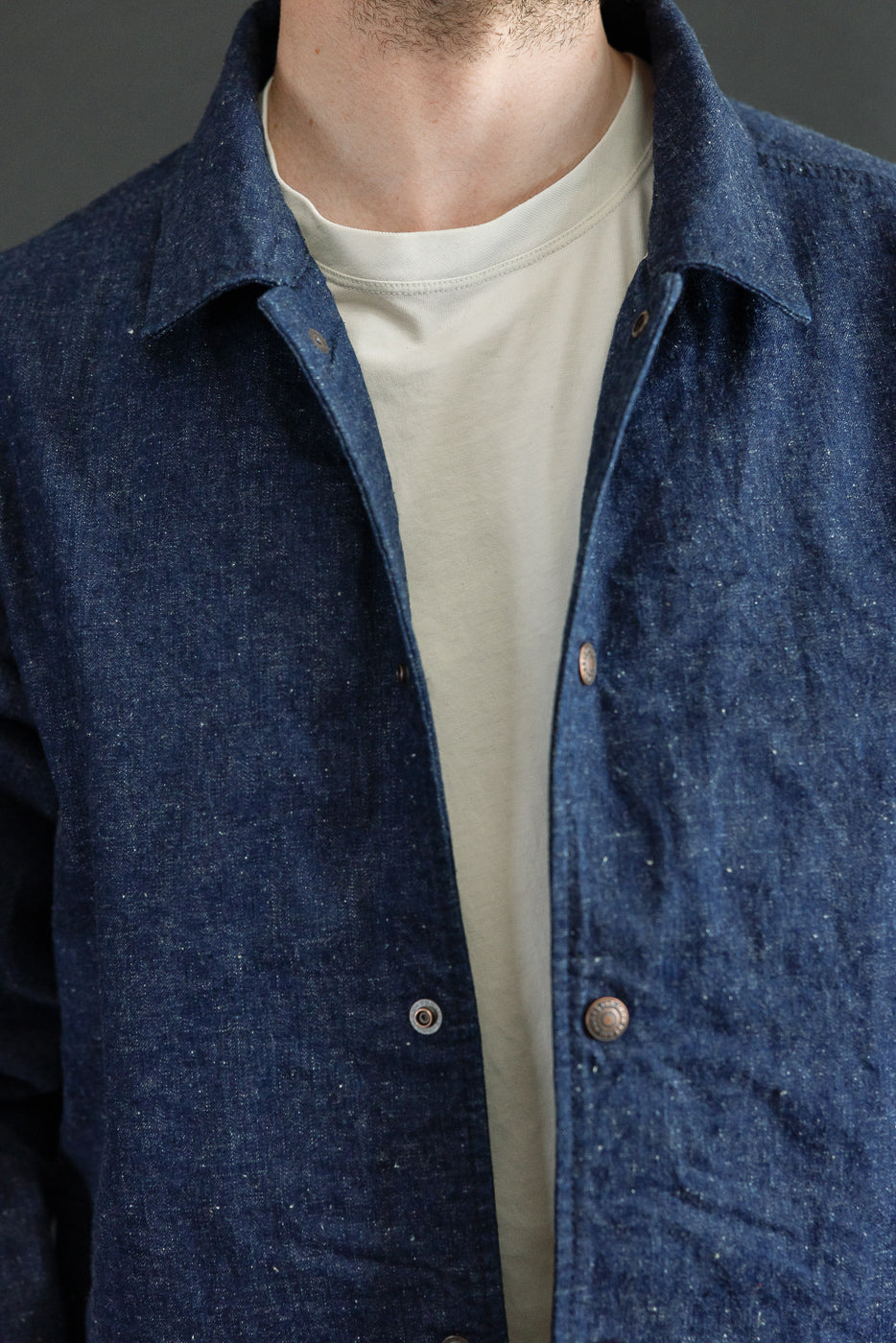 Close-up front view of male model in indigo denim shirt with button details, collar, and textured fabric