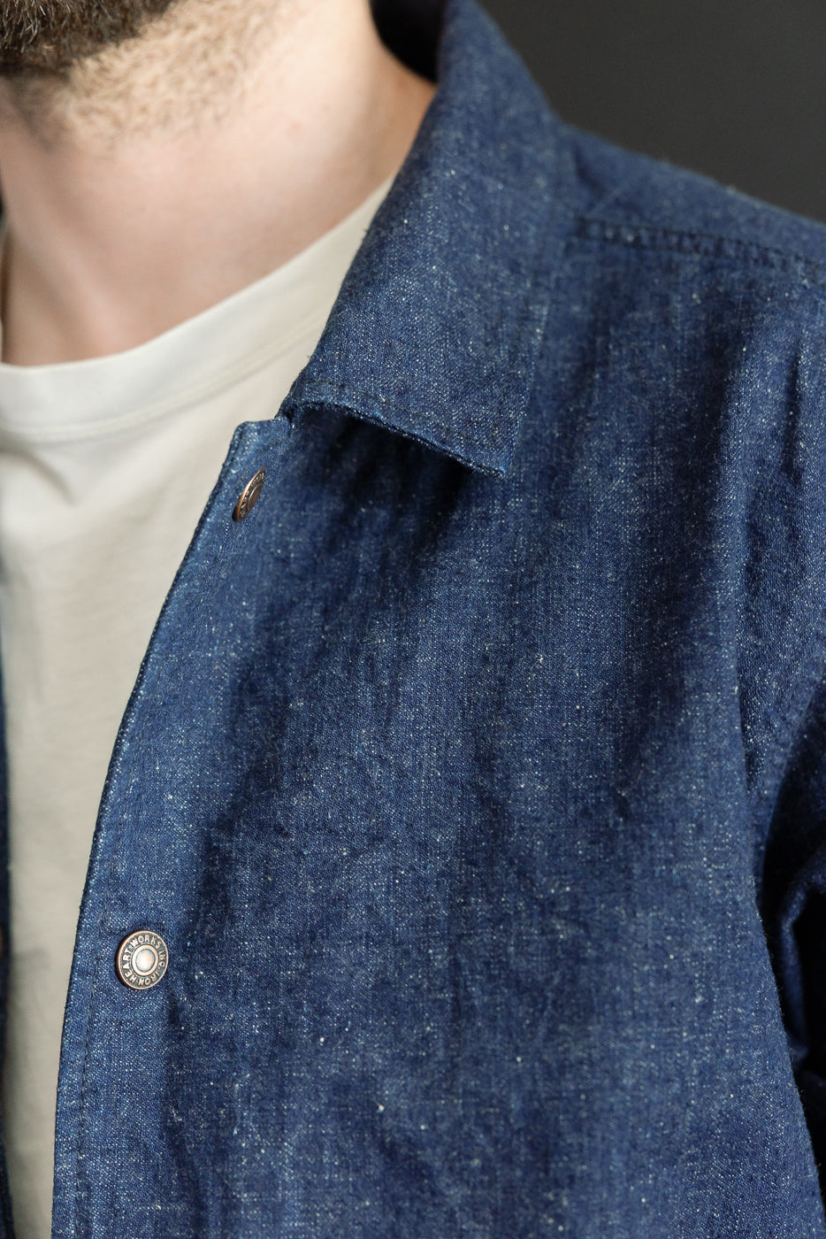 Close-up front view of male model wearing indigo denim shirt with button collar, visible texture, and branded buttons